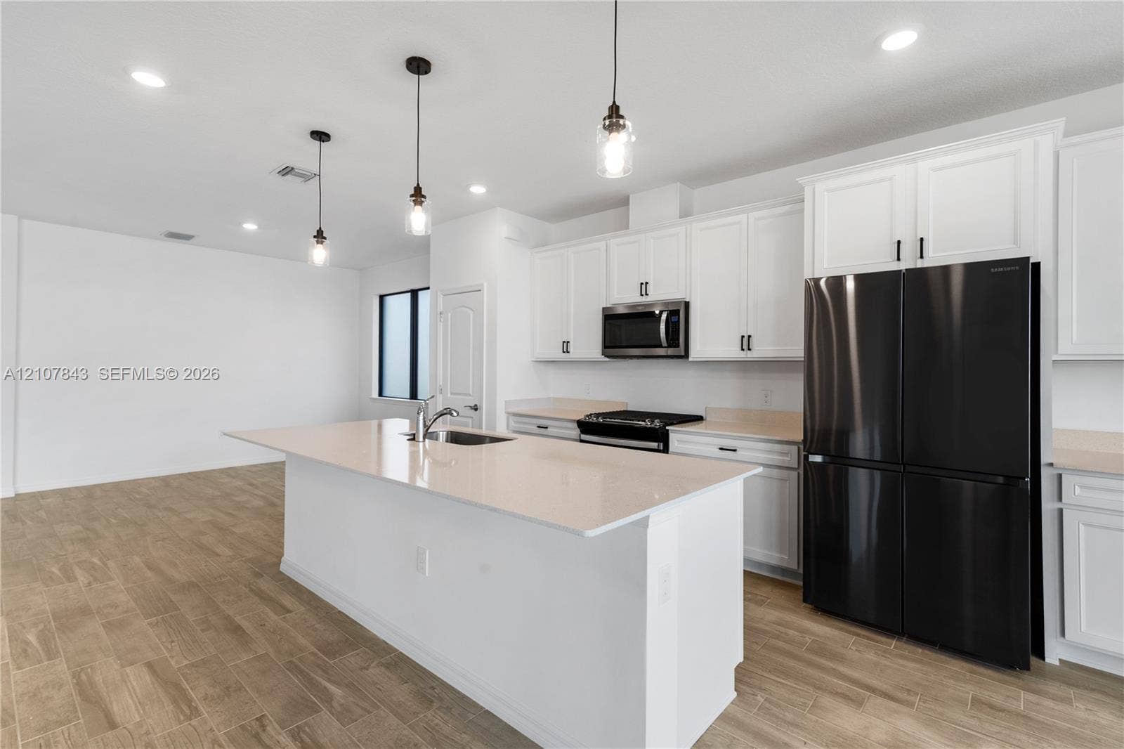 4949 Blistering Way, Lake Worth, FL 33467 Kitchen featuring white cabinetry, an expansive central island with a sink, quartz-style countertops, wood-finish flooring, and pendant lighting
