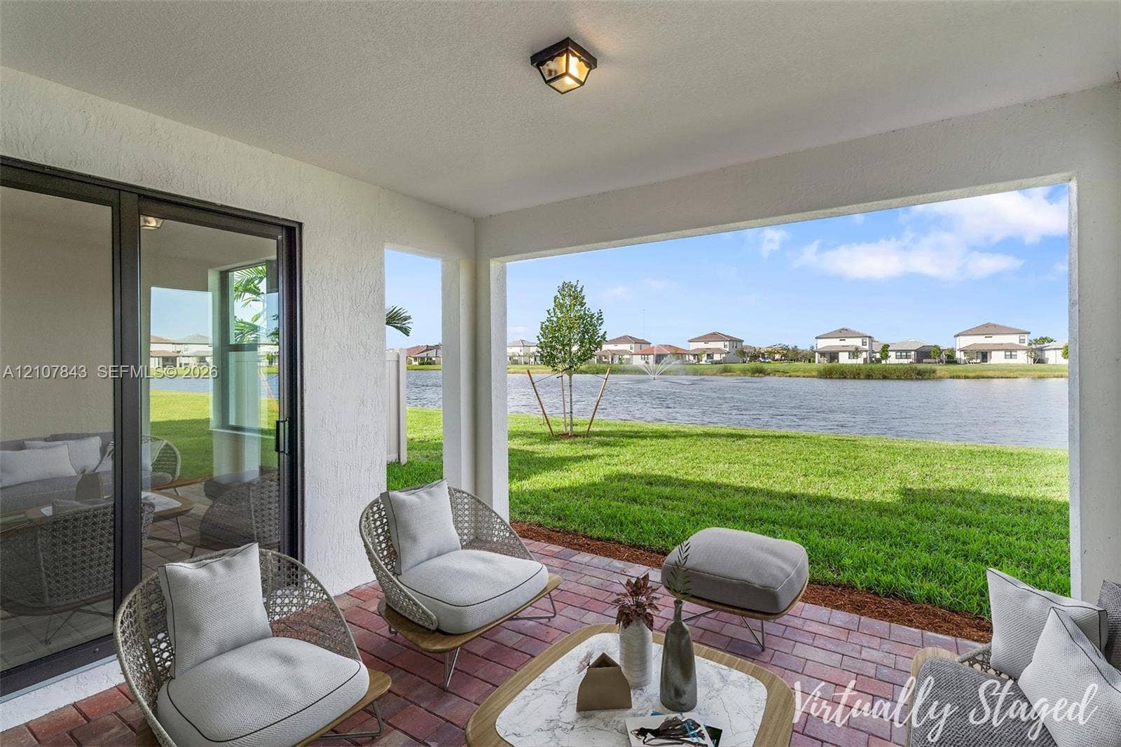 4949 Blistering Way, Lake Worth, FL 33467 Covered patio featuring red brick paving, flush-mount lighting, and large sliding glass doors, opening to a grass lawn and water frontage