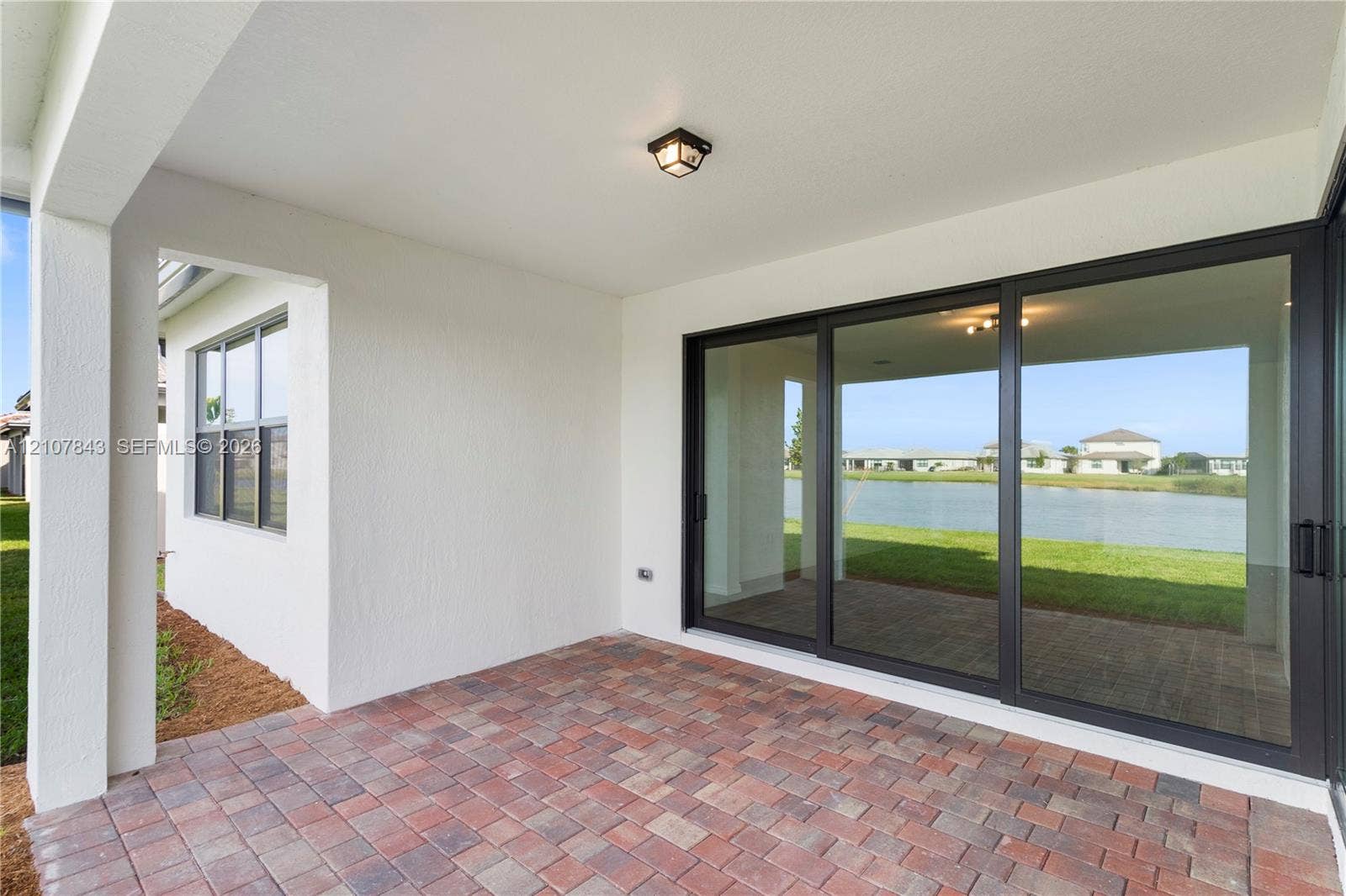 4949 Blistering Way, Lake Worth, FL 33467 Covered patio featuring multi-tone paver flooring, dark-framed sliding glass doors, and a flush-mount light fixture