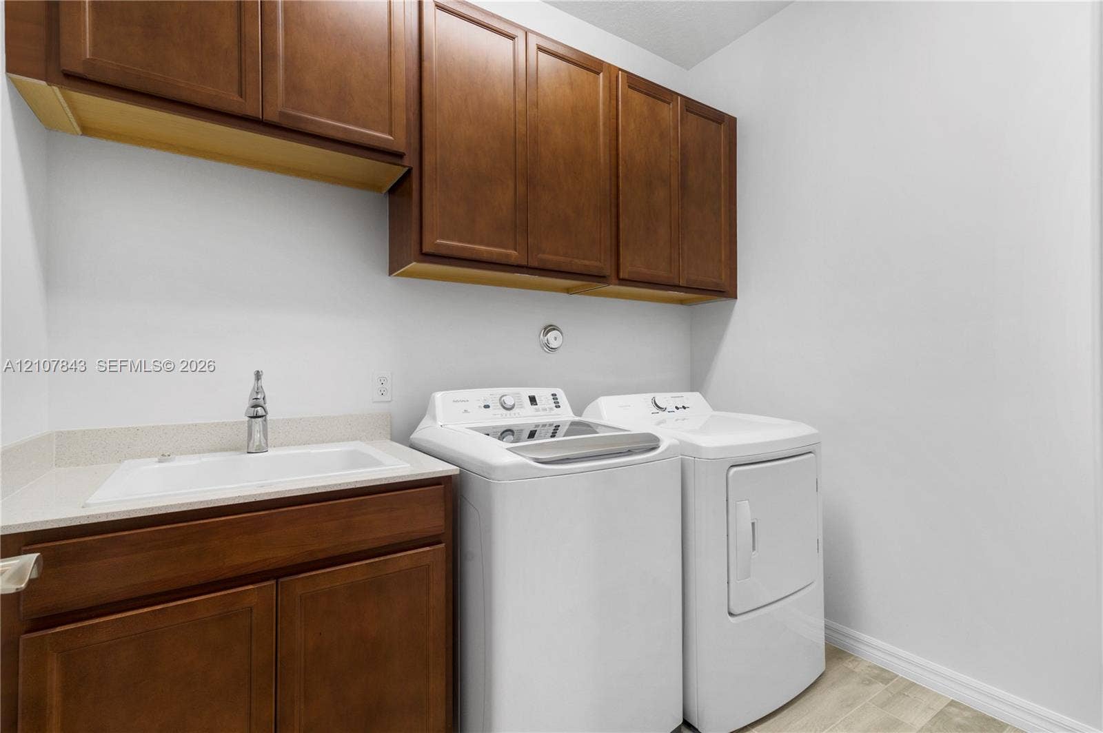 4949 Blistering Way, Lake Worth, FL 33467 Laundry room featuring stained wood cabinetry, a solid surface countertop, a drop-in basin sink with a metal faucet, and wood-finish flooring