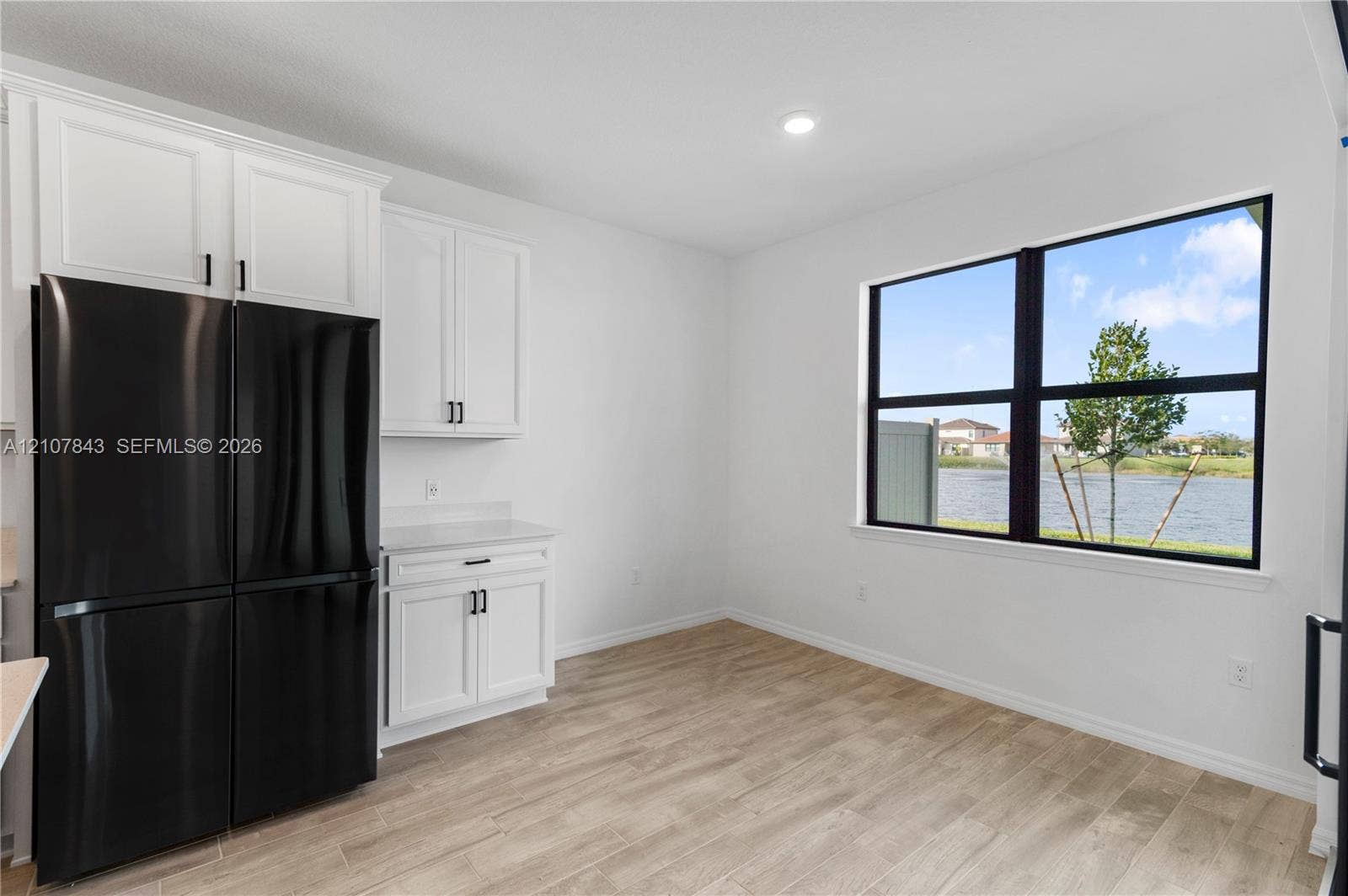 4949 Blistering Way, Lake Worth, FL 33467 White shaker-style cabinetry, matte black hardware, wood-finish flooring, integrated black refrigerator, and large window with water scenery