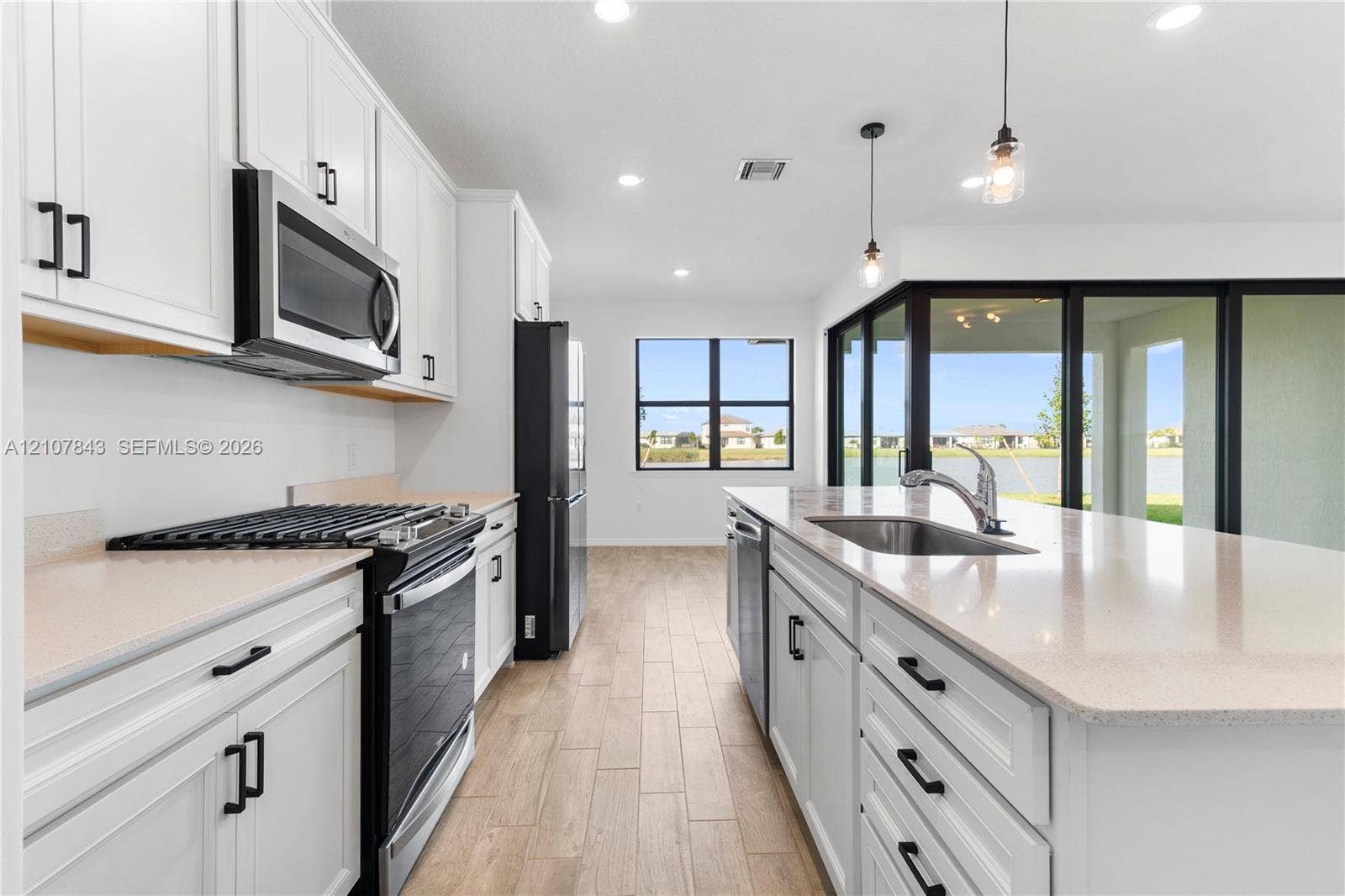 4949 Blistering Way, Lake Worth, FL 33467 Kitchen featuring white shaker-style cabinetry, quartz countertops, stainless steel appliances, a center island with a stainless steel sink, and wood-finish flooring