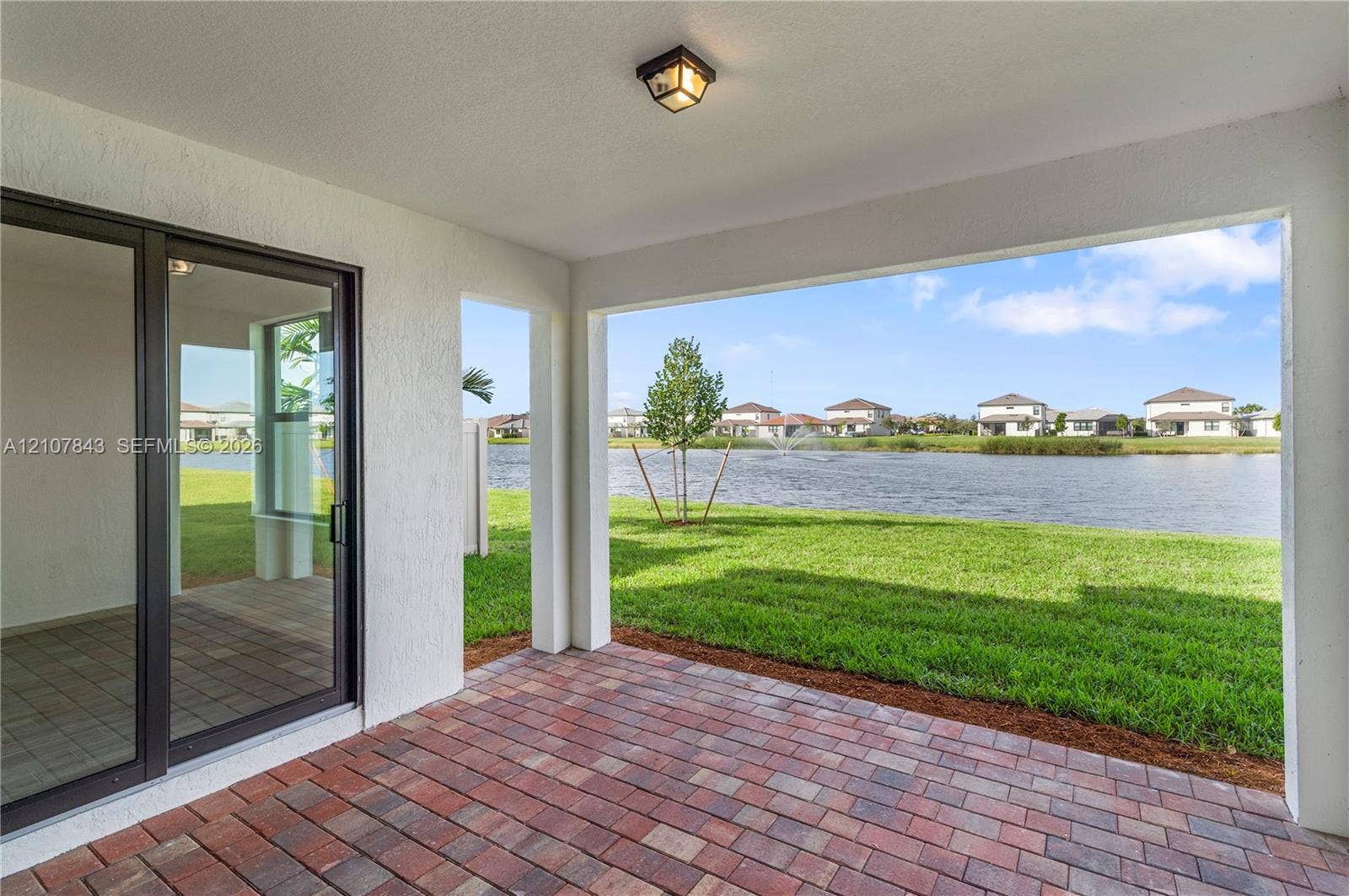 4949 Blistering Way, Lake Worth, FL 33467 Covered concrete patio with multi-toned brick-style pavers, flush-mount lighting, and large sliding glass door entry overlooking a pond