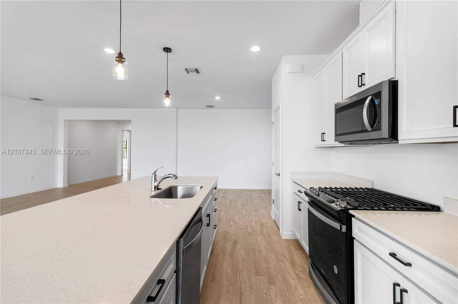 4949 Blistering Way, Lake Worth, FL 33467 Kitchen featuring white shaker-style cabinetry, solid-surface countertops, a center island with an undermount sink, recessed lighting, and wood-finish flooring