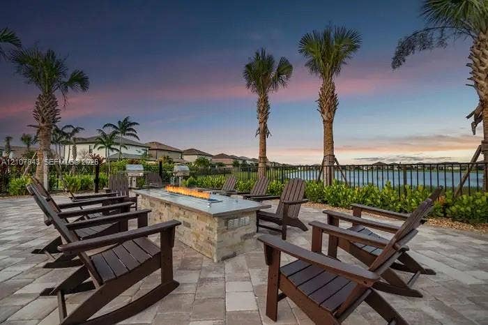 4949 Blistering Way, Lake Worth, FL 33467 Rear patio featuring a stone-clad fire table, paver hardscaping, metal perimeter fencing, and mature palm trees