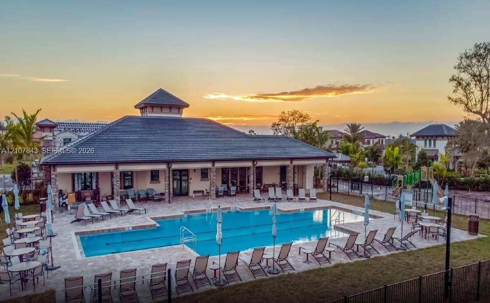 4949 Blistering Way, Lake Worth, FL 33467 Community recreation center featuring a rectangular swimming pool with paved decking, a covered veranda, stone pillar accents, and a multi-sloped roofline