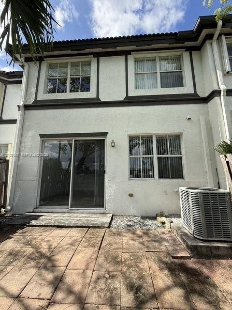 Exterior rear elevation featuring a stucco facade with dark trim, dual-pane multi-light windows, sliding glass door, and a paver patio