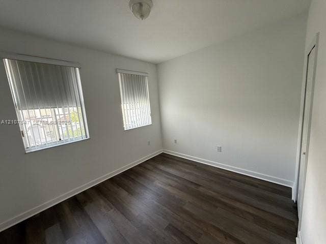 Neutral interior walls with wood-finish flooring, dual windows with vertical blinds, and a built-in closet with sliding doors