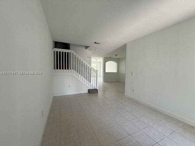 Open-concept interior featuring neutral tile flooring, white walls, a staircase with a white railing, and a decorative archway