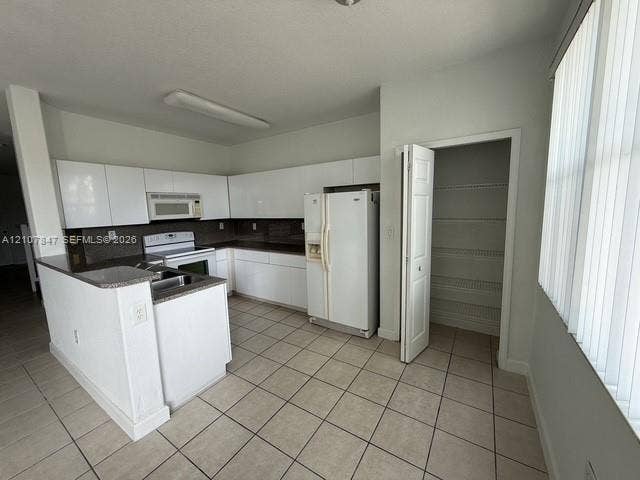 Kitchen featuring white cabinetry, dark countertops, tiled flooring, an integrated pantry, and a peninsula