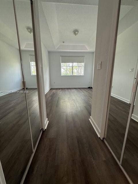 Room featuring wood-finish flooring, a tray ceiling, dual mirrored sliding closet doors, and a window with a roller shade