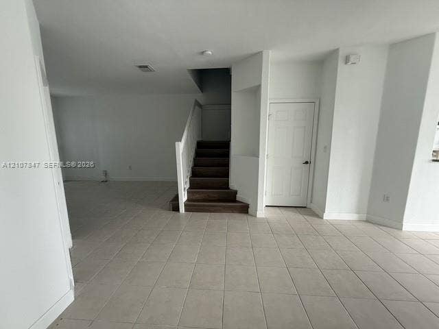 Neutral-toned ceramic tile flooring, staircase with wood-finish treads, white handrail, and built-in recessed wall niche