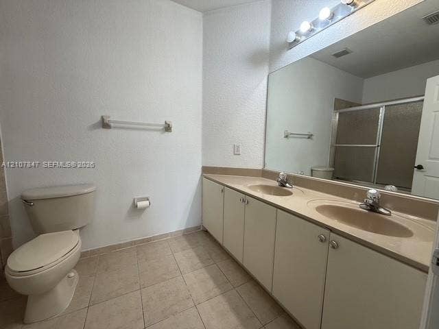 Dual-sink vanity with solid-surface integrated countertops, full-width vanity mirror, tile flooring, and a combined tub and shower enclosure with a sliding glass door