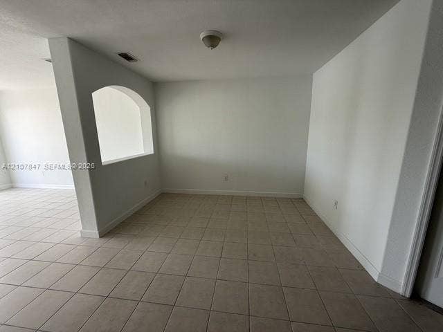 Interior space featuring neutral tile flooring, smooth white walls, a structural arched wall cutout, and a ceiling-mounted light fixture