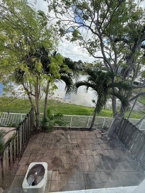 Paved patio featuring a water-front location, perimeter wood fencing, and mature trees