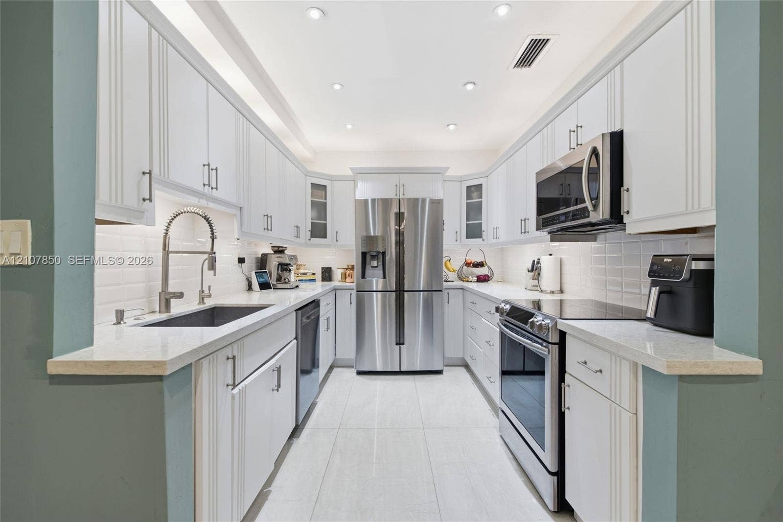 Galley kitchen featuring white cabinetry, light-toned stone-finish countertops, stainless steel appliances, a white tile backsplash, and recessed lighting
