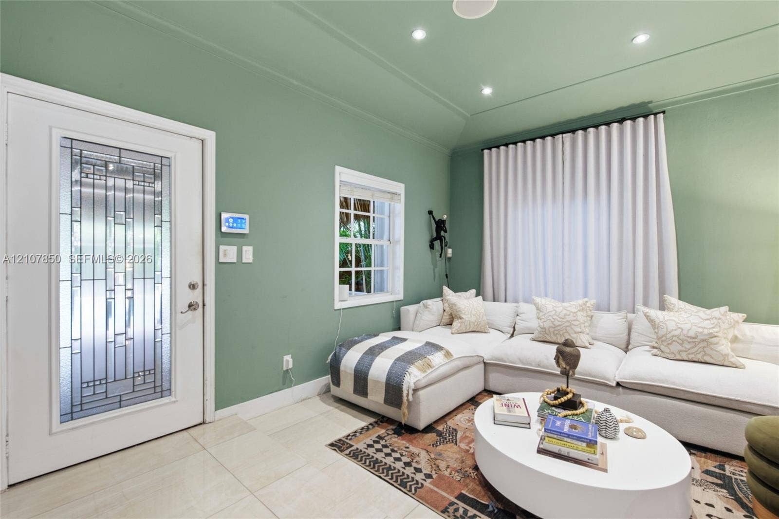 Entry area featuring a glass-inset door with geometric detailing, recessed ceiling lighting, tray ceiling architecture, large-format tile flooring, and a multi-pane window