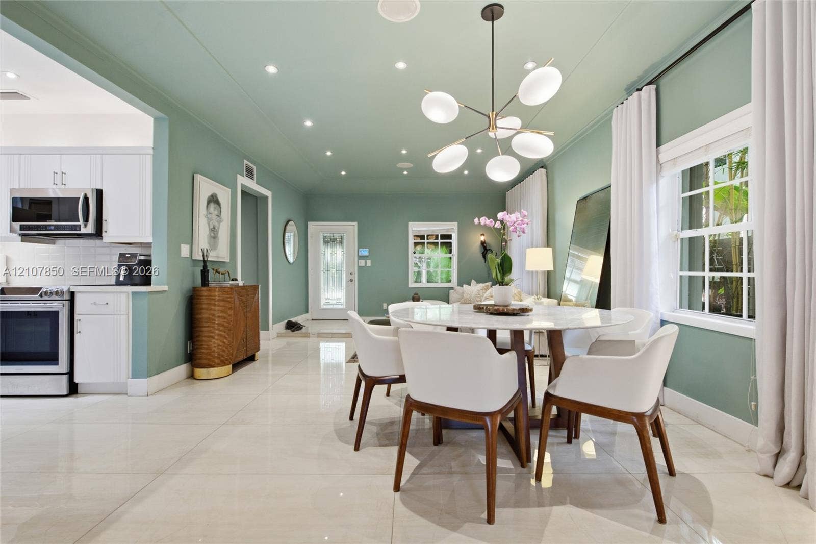 Open-concept living space featuring high-gloss tile flooring, recessed lighting, a modern multi-globe chandelier, and a kitchen equipped with white cabinetry and stainless steel appliances