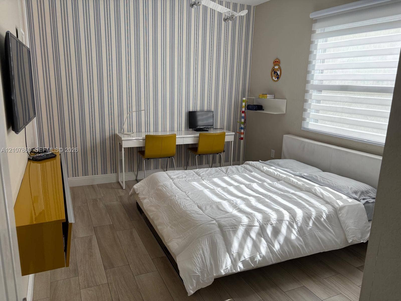 8925 NW 99th Court, Doral, FL 33178 Wood-finish flooring, vertical-striped accent wall, built-in mustard-tone wall cabinetry, and light-filtering horizontal window shades