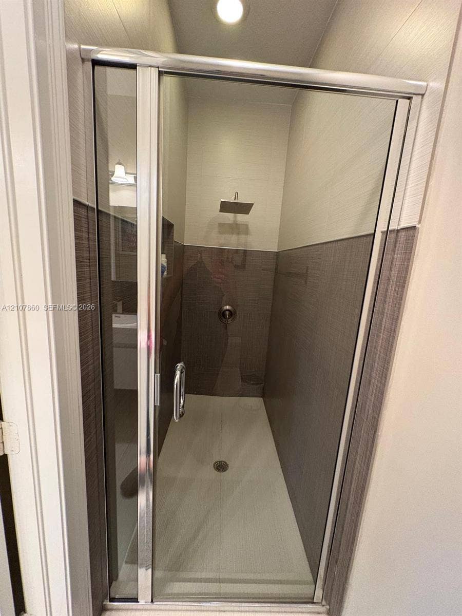 8925 NW 99th Court, Doral, FL 33178 Walk-in shower featuring a glass enclosure with a silver-finish frame, a square rainfall showerhead, integrated wall niche, and two-tone horizontal tile surround