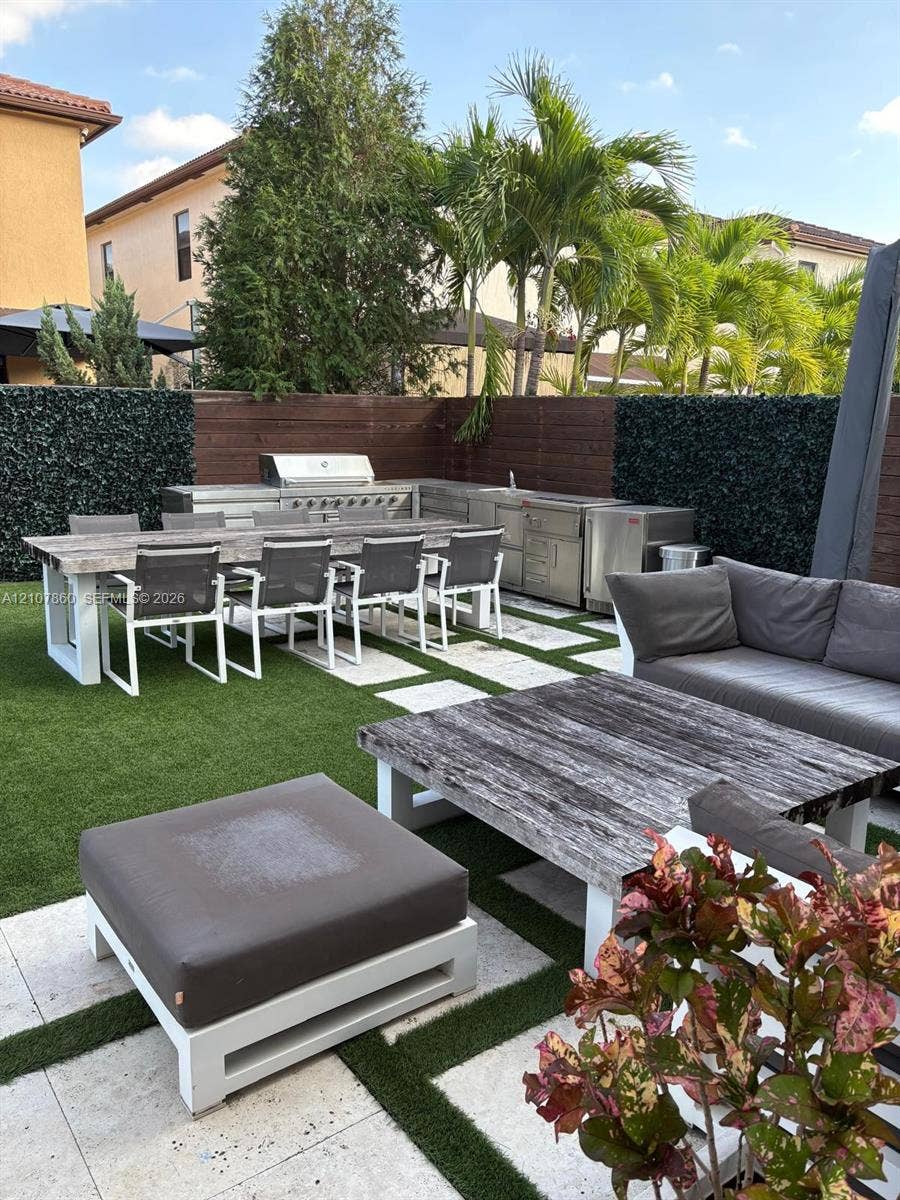 8925 NW 99th Court, Doral, FL 33178 Outdoor kitchen featuring stainless steel appliances and a built-in grill, complemented by paver stone hardscaping, artificial turf, and wood privacy fencing