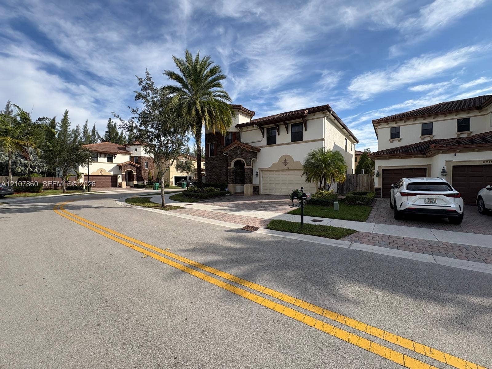 8925 NW 99th Court, Doral, FL 33178 Two-story exterior featuring a stucco facade with decorative stone accents, a tiled roof, paver driveway, and an attached multi-car garage