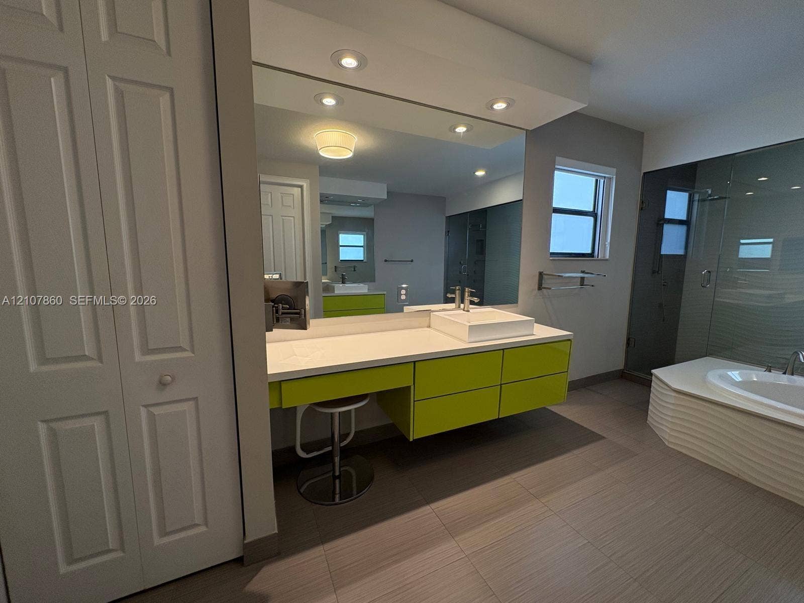 8925 NW 99th Court, Doral, FL 33178 Floating vanity with a rectangular vessel sink and solid-surface countertop, full-width mirror, recessed lighting, tile flooring, and a glass-enclosed shower with a soaking tub
