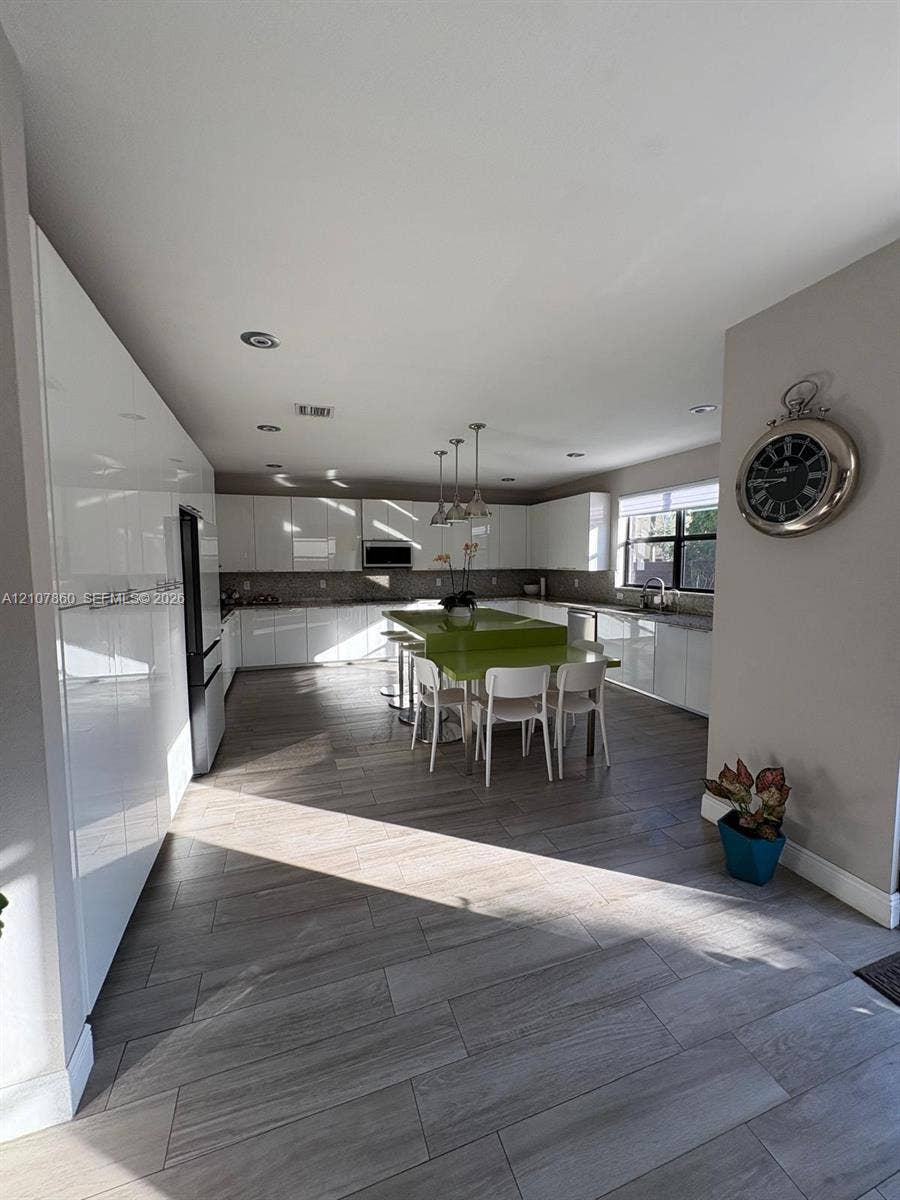 8925 NW 99th Court, Doral, FL 33178 Kitchen featuring high-gloss white cabinetry, wood-finish flooring, a central island with a solid-surface countertop, recessed lighting, and stainless-steel built-in appliances