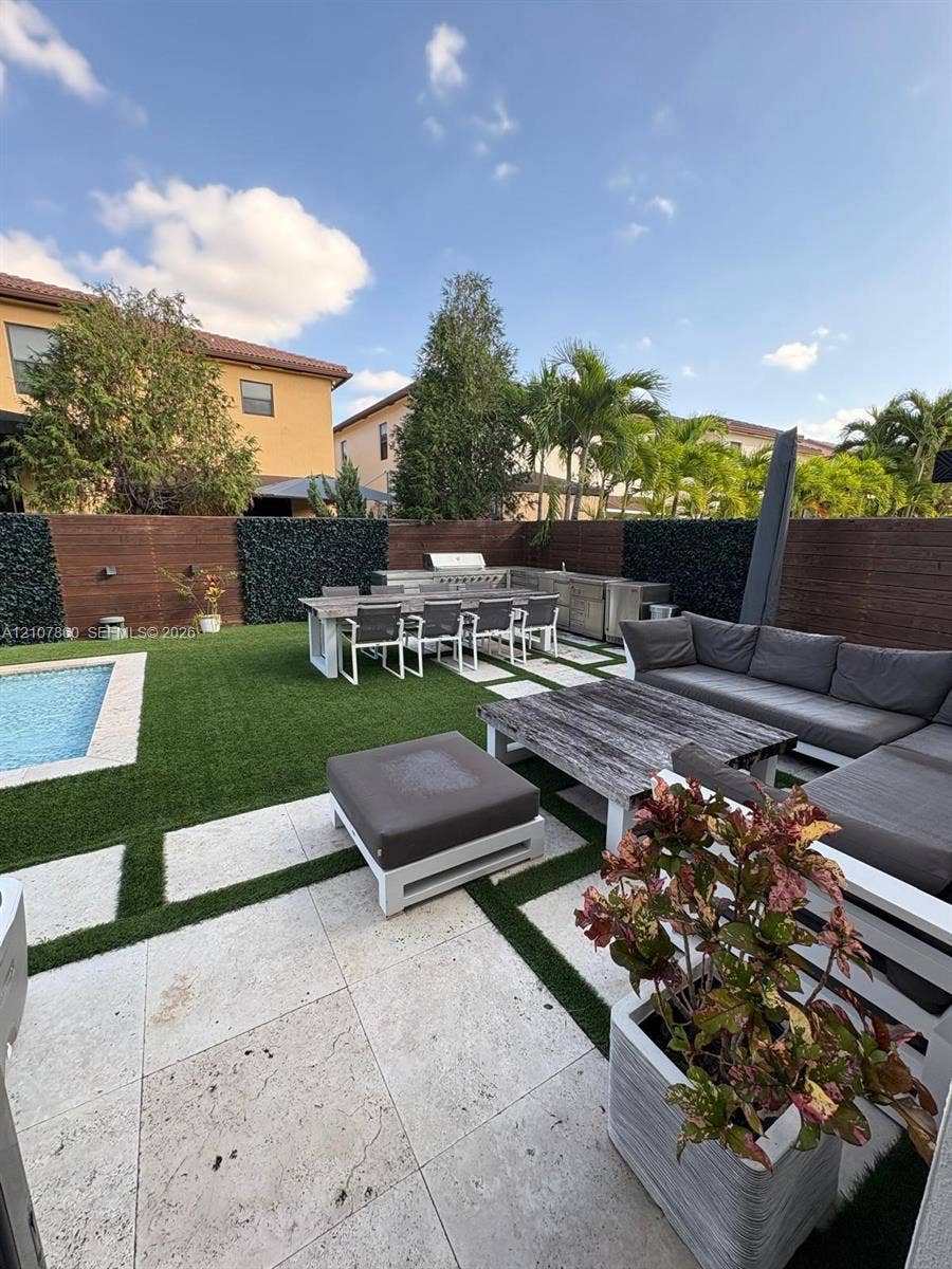 8925 NW 99th Court, Doral, FL 33178 Backyard area featuring a swimming pool, stone paver decking with grass inlay, built-in outdoor kitchen, and tall privacy fencing