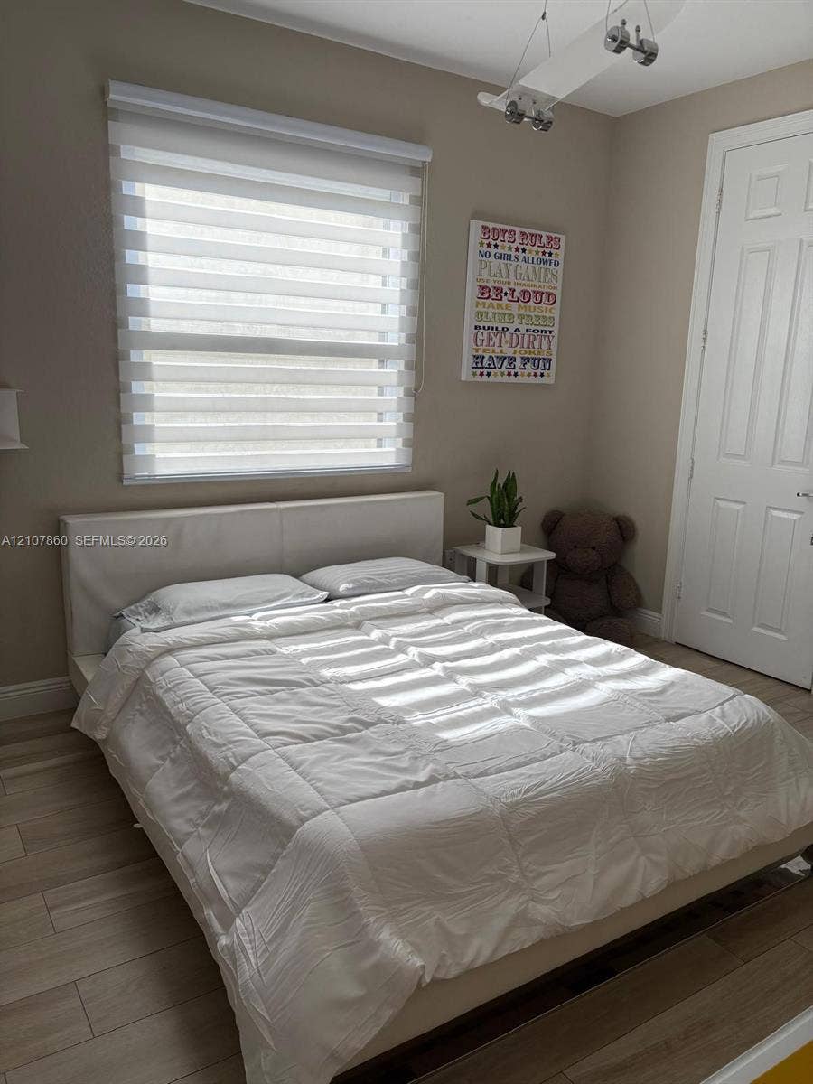 8925 NW 99th Court, Doral, FL 33178 Neutral-toned room featuring wood-finish flooring, a multi-panel door, installed ceiling-mounted track lighting, and a roller shade window treatment