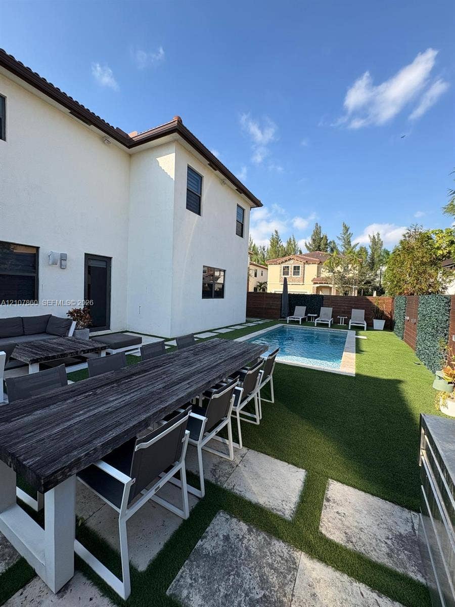 8925 NW 99th Court, Doral, FL 33178 Backyard featuring an in-ground swimming pool, synthetic turf lawn, stone paver accents, and perimeter privacy fencing