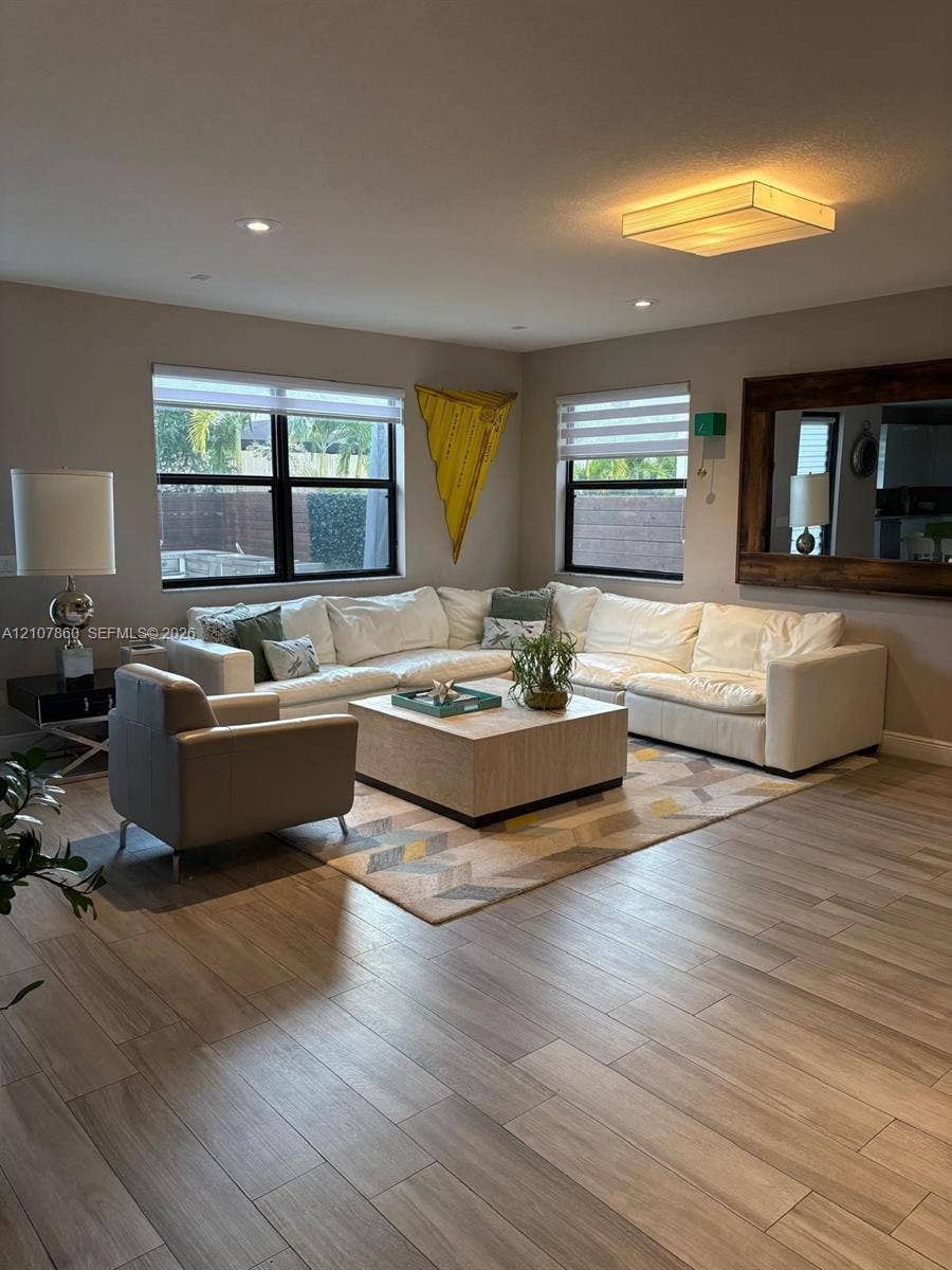 8925 NW 99th Court, Doral, FL 33178 Wood-finish tile flooring, recessed lighting, large rectangular flush-mount ceiling fixture, dual-pane windows with black frames, and a large wall-mounted mirror with a wide wood frame