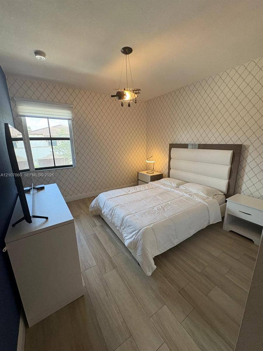 8925 NW 99th Court, Doral, FL 33178 Room featuring patterned wall covering, wood-finish flooring, and a multi-light pendant fixture