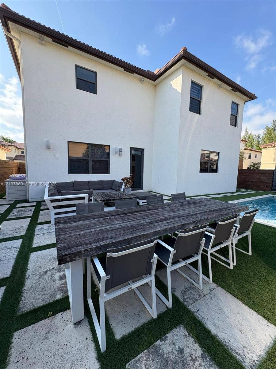 8925 NW 99th Court, Doral, FL 33178 Stucco exterior with a multi-level roofline, swimming pool, and geometric paver patio with integrated synthetic turf