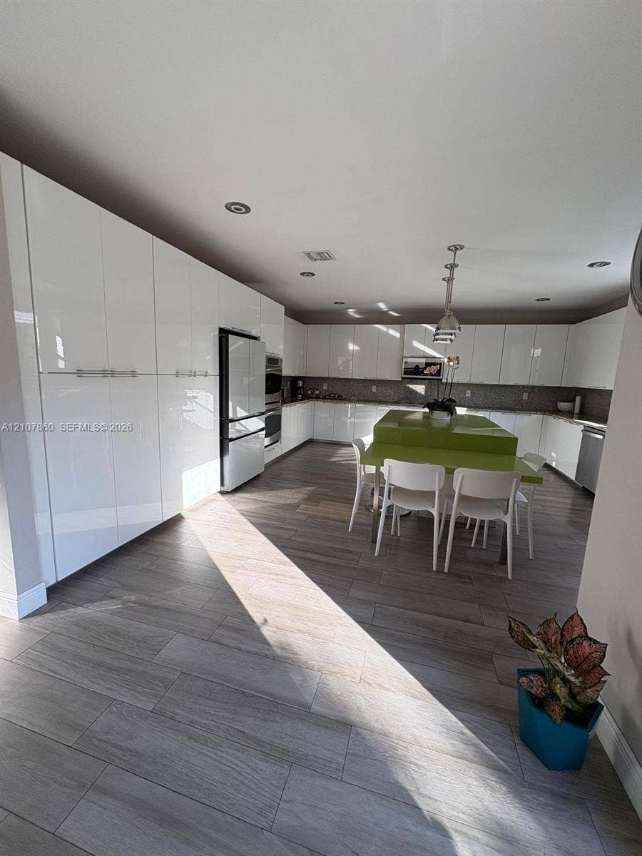 8925 NW 99th Court, Doral, FL 33178 Kitchen featuring high-gloss white cabinetry, expansive stone-surface center island, wood-finish tile flooring, recessed ceiling lighting, and stainless steel built-in appliances