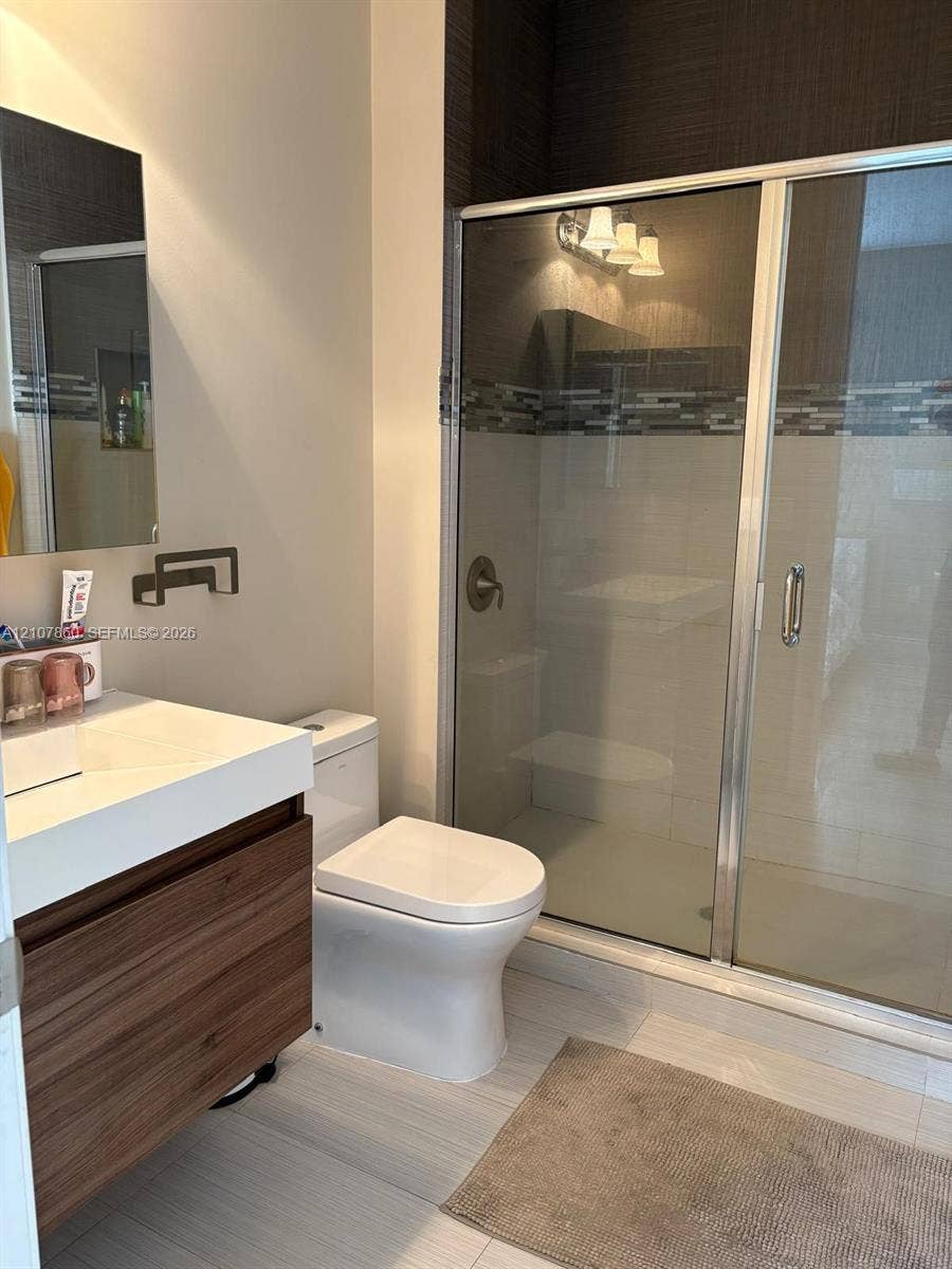8925 NW 99th Court, Doral, FL 33178 Floating vanity with wood-finish cabinetry, rectangular countertop basin, walk-in shower with glass enclosure, decorative tile inlay, and neutral tile flooring