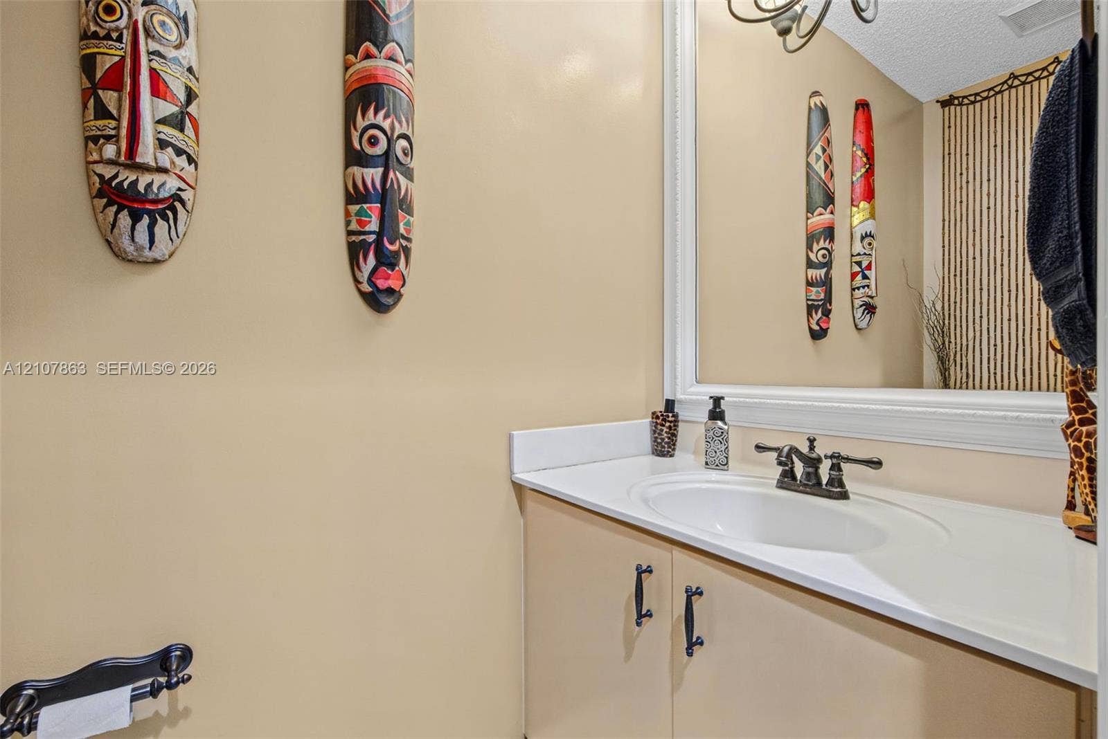 Bathroom vanity featuring a solid-surface countertop with an integrated oval sink, oil-rubbed bronze double-handle faucet, white framed mirror, and matte black cabinet pulls