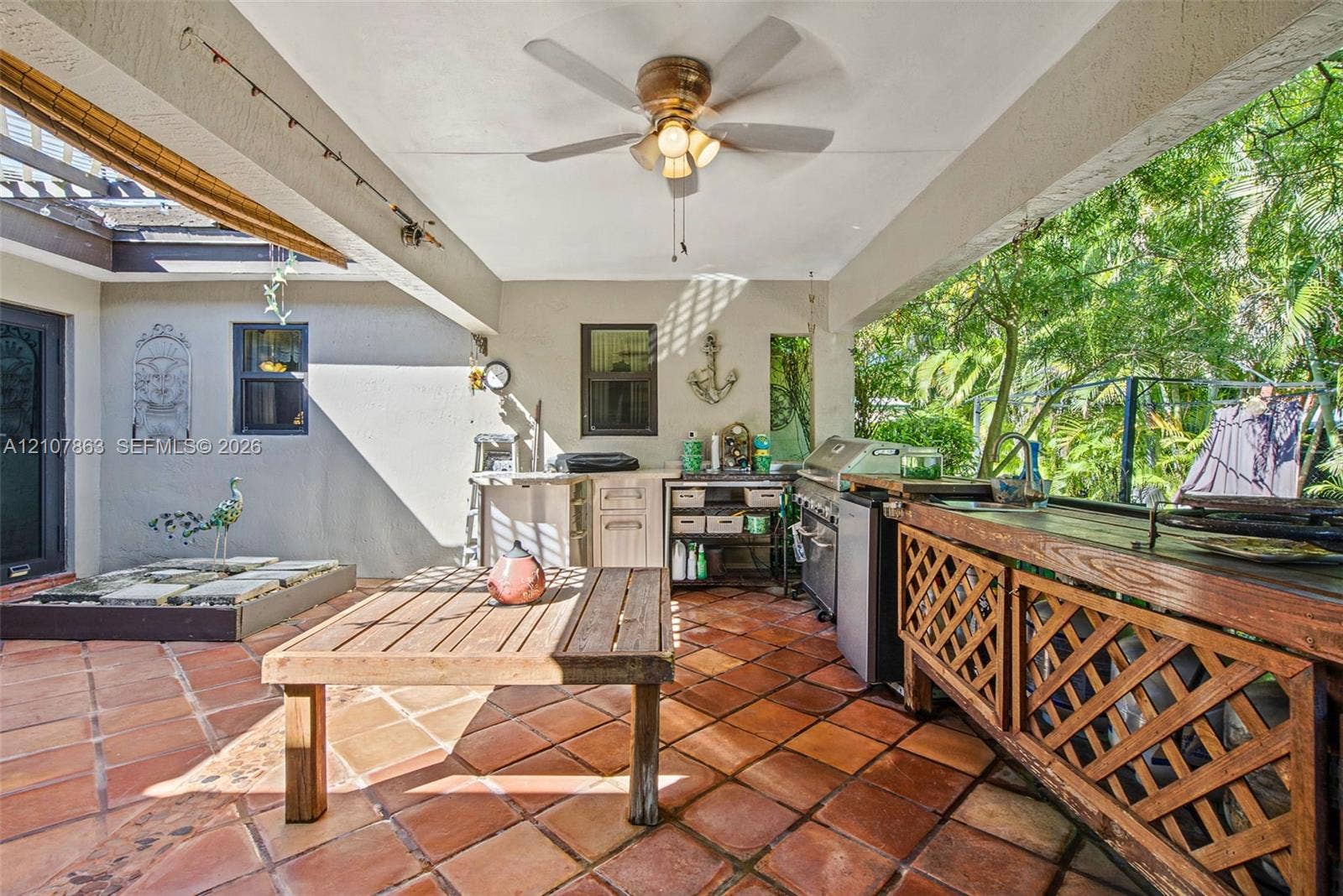 Covered outdoor kitchen featuring tile flooring, built-in cabinetry, stainless steel grill, and ceiling fan