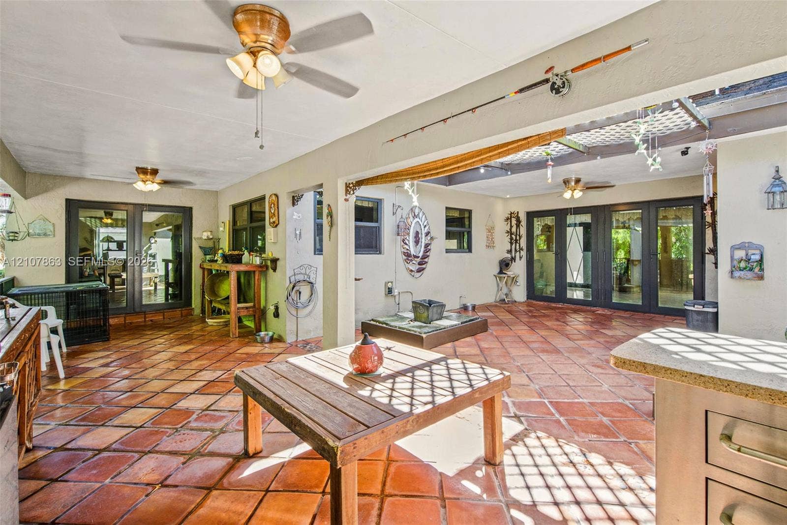 Covered outdoor patio featuring terra cotta tile flooring, multi-pane glass doors, built-in cabinetry, and dual ceiling fans