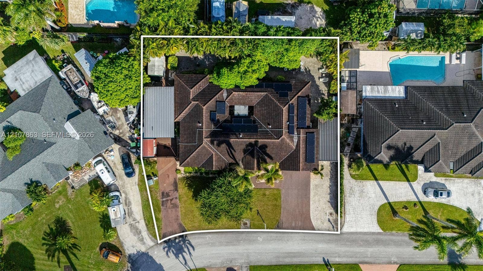 Aerial perspective of a property featuring a multi-gabled roof, paved driveways, established trees, and solar panel arrays