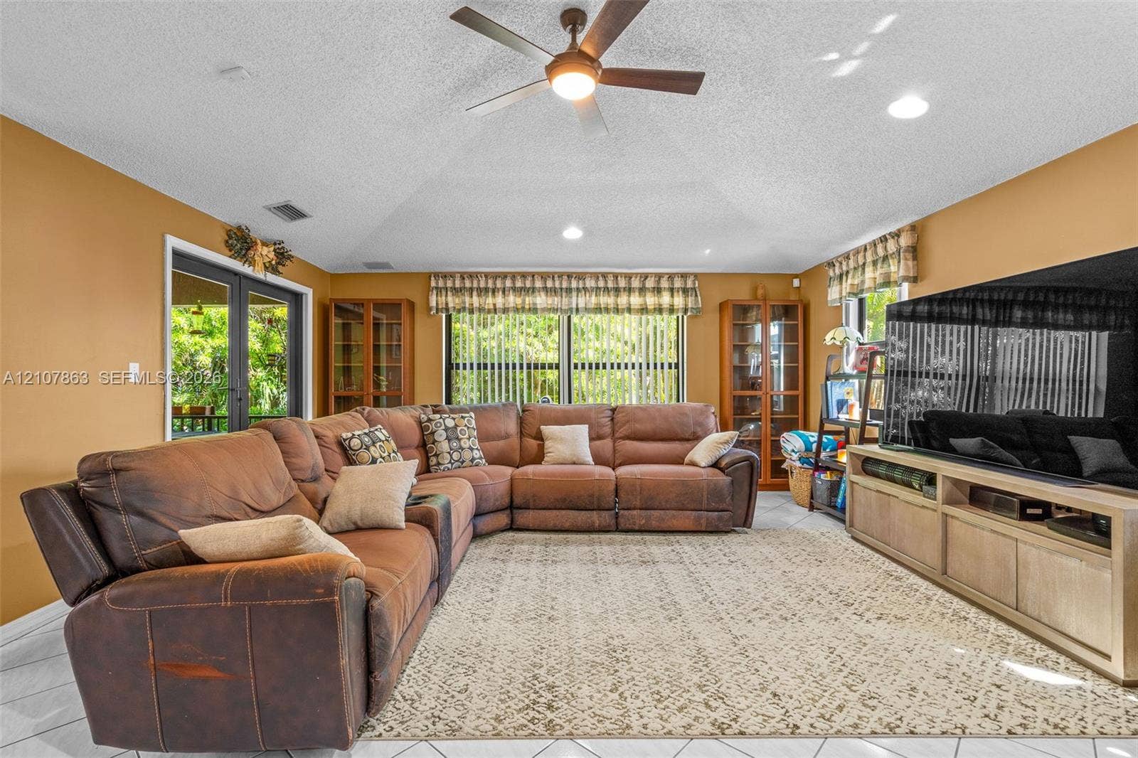 Vaulted ceilings featuring a central overhead fan, tile flooring, built-in display cabinetry, and double glass-paneled exterior doors
