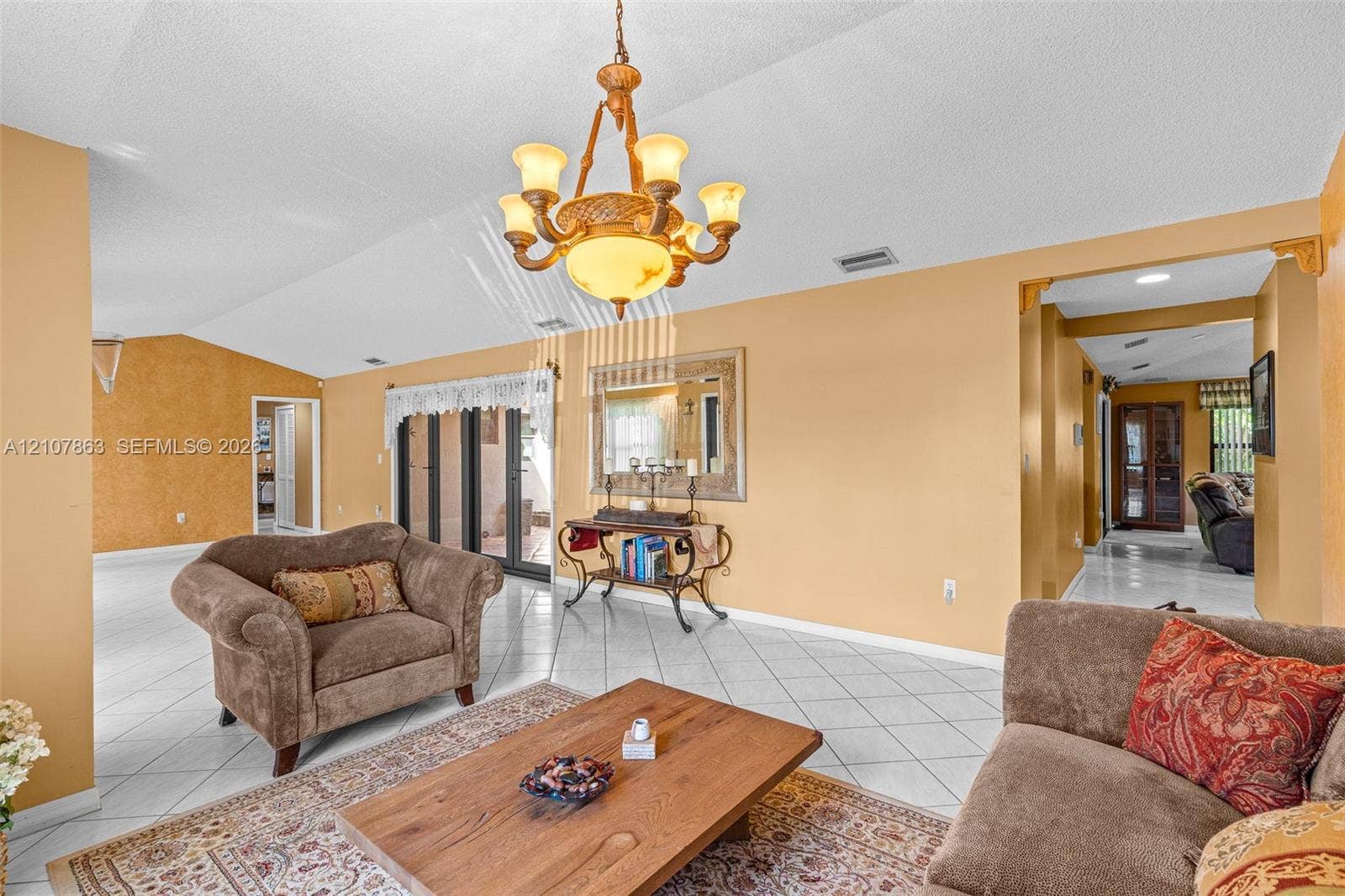 Vaulted ceilings, large-format tile flooring, multi-arm metal chandelier, and wall-mounted decorative mirror