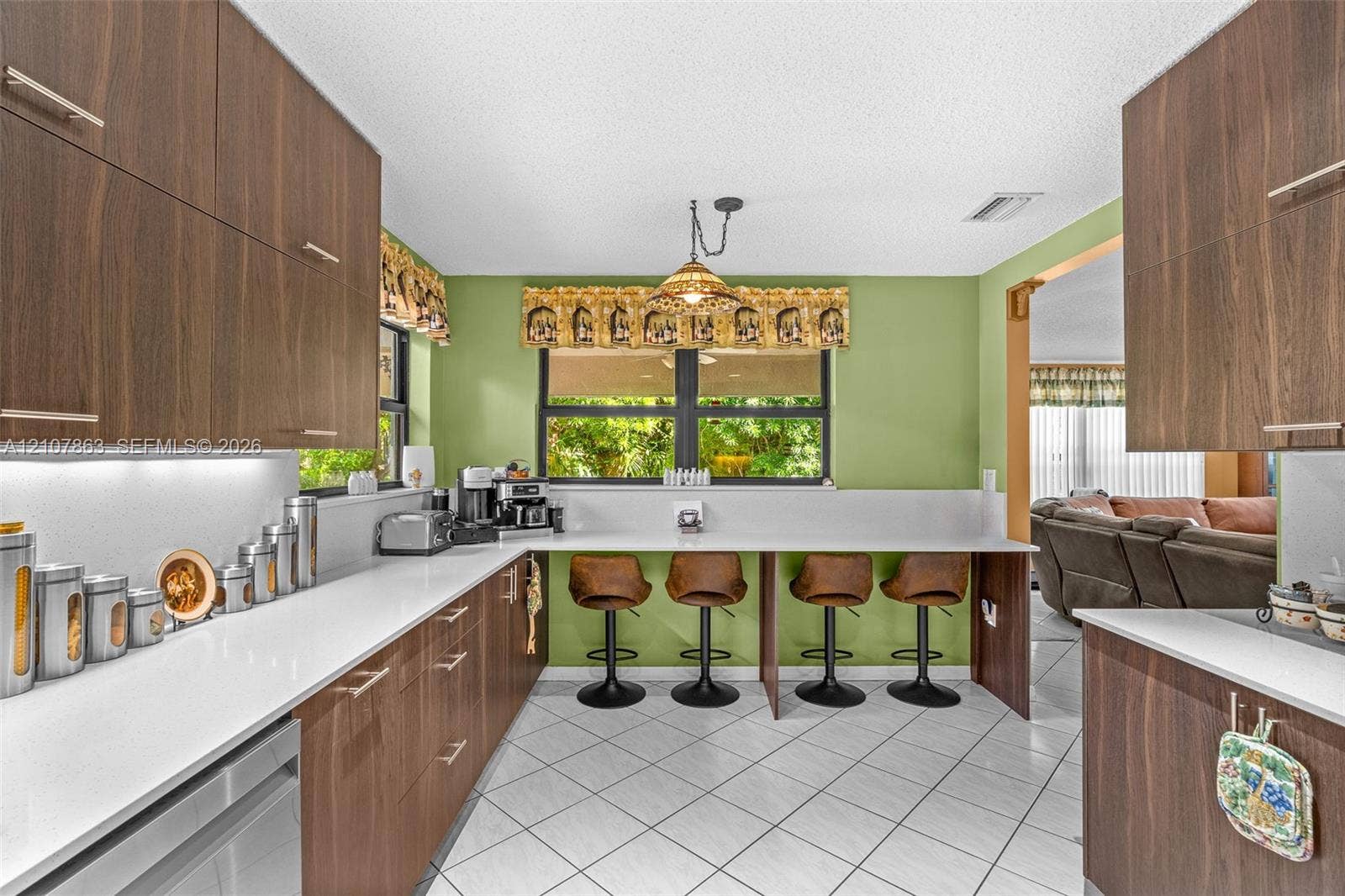 Kitchen featuring flat-panel wood-finish cabinetry, white solid-surface countertops, tile flooring, and a built-in breakfast bar