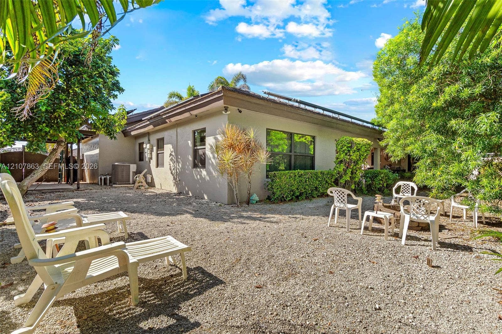 Exterior side yard featuring gravel ground cover, mature landscaping, dark-trimmed roofline, and low-maintenance stucco siding