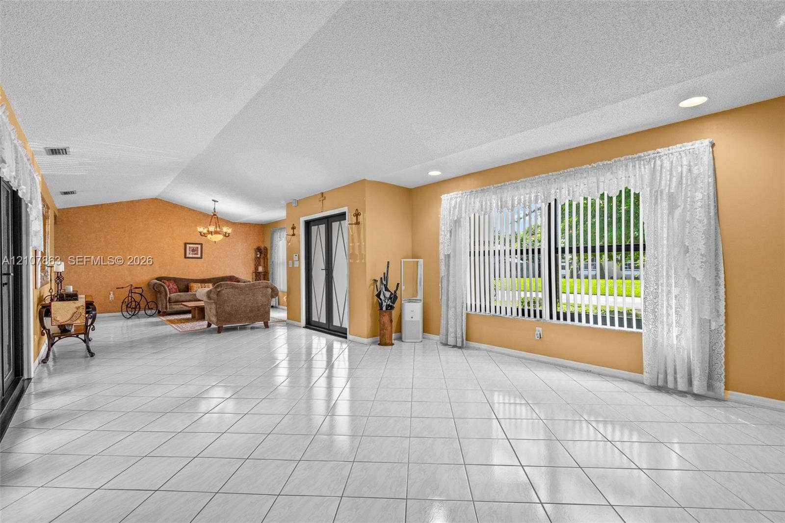 Spacious interior featuring ceramic tile flooring, vaulted ceilings, recessed lighting, a multi-pane glass entry door, and large windows with vertical blinds
