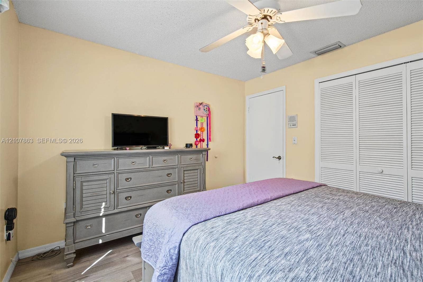 Bedroom featuring wood-finish flooring, a ceiling fan with integrated lighting, and a closet with white louvered doors