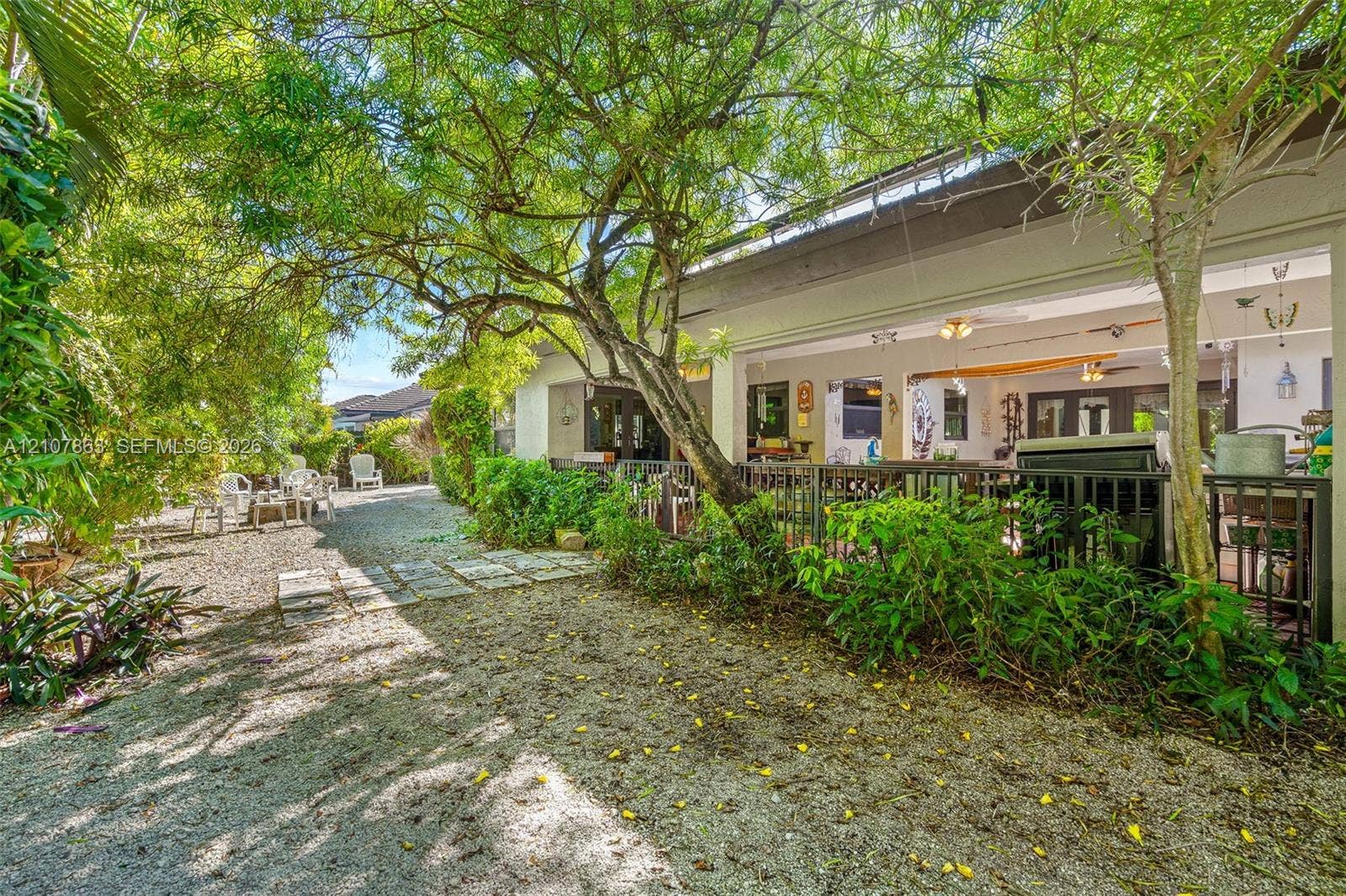 Landscaped backyard featuring crushed stone ground cover, mature trees, ornamental shrubs, and a metal perimeter fence