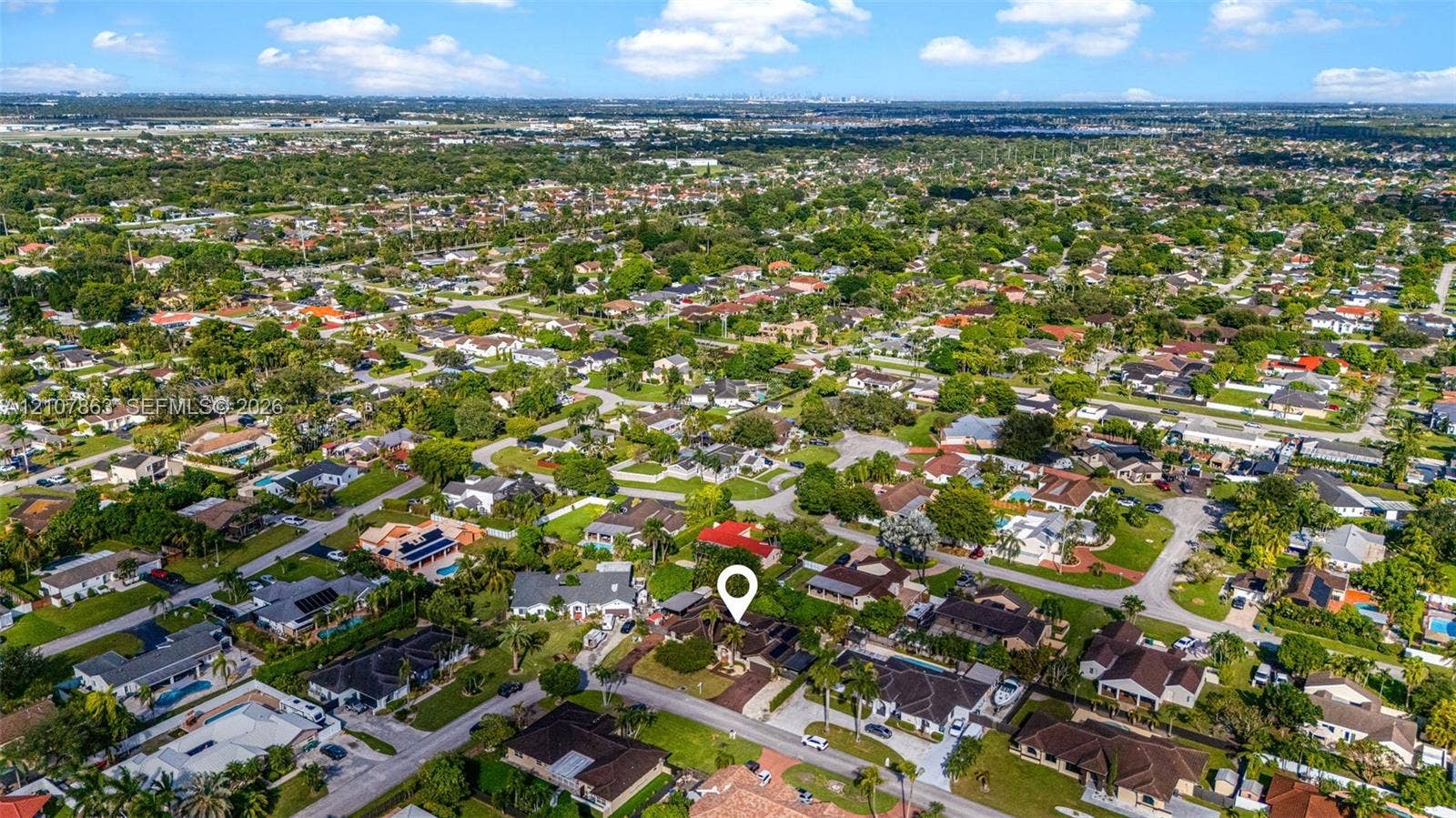 Aerial view of a residential property featuring a dedicated driveway, expansive lawn, mature landscaping, and multi-pitched roofline