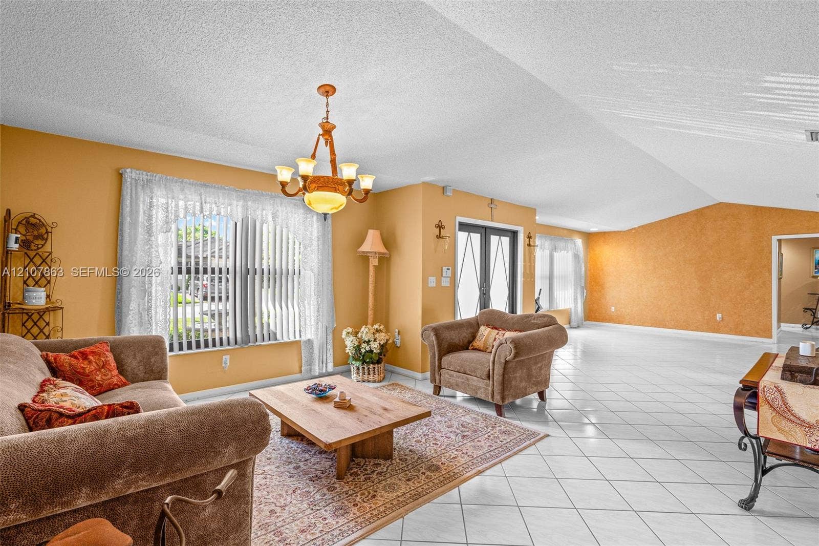Vaulted ceilings, expansive tile flooring, large windows with vertical blinds, and a multi-arm chandelier