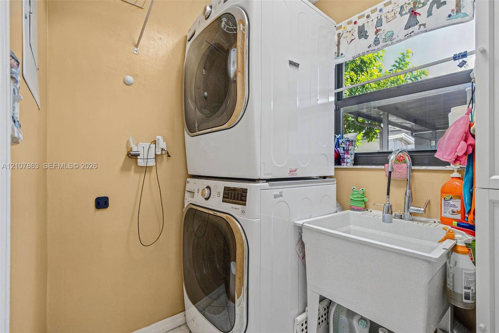 Laundry area featuring a stackable washer and dryer, a deep utility sink with a pull-down faucet, and a large window